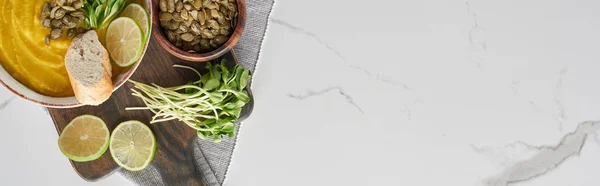 Panoramic shot of delicious mashed pumpkin soup on wooden cutting board on marble surface with ingredients — Stock Photo