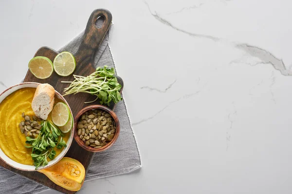 Vue de dessus de la délicieuse soupe à la citrouille écrasée sur planche à découper en bois sur la surface de marbre avec des ingrédients — Photo de stock