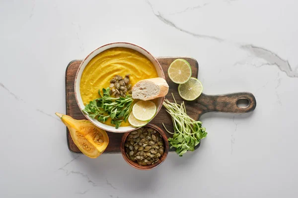 Vue de dessus de la délicieuse soupe à la citrouille écrasée sur planche à découper en bois sur la surface de marbre avec des ingrédients — Photo de stock