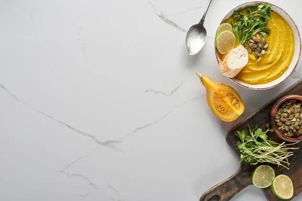 Vista superior da deliciosa sopa de abóbora purê na placa de corte de madeira na superfície de mármore com ingredientes — Fotografia de Stock