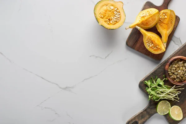 Vista dall'alto di zucca, lime, germogli. semi su tagliere in legno su superficie marmorea — Foto stock