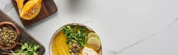 Panoramic shot of autumnal mashed pumpkin soup on wooden cutting board on marble surface — Stock Photo