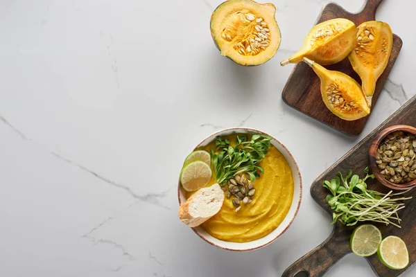 Top view of tasty mashed pumpkin soup on wooden cutting board with ingredients on marble surface — Stock Photo