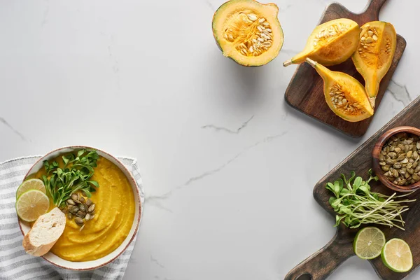 Top view of tasty mashed pumpkin soup on wooden cutting board with ingredients on marble surface — Stock Photo