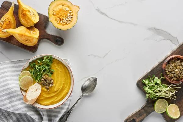 Vista superior da sopa de abóbora triturada saborosa na placa de corte de madeira com ingredientes na superfície de mármore — Fotografia de Stock