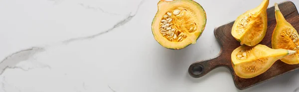 Top view of cut pumpkin on wooden cutting board on marble surface, panoramic shot — Stock Photo