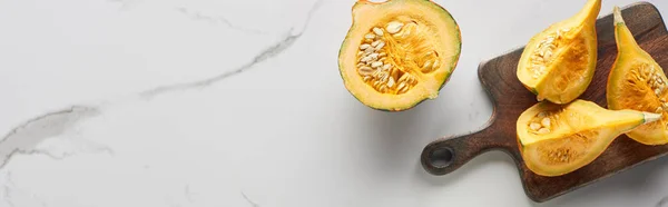 Vue de dessus de citrouille coupée sur planche à découper en bois sur surface de marbre, vue panoramique — Photo de stock