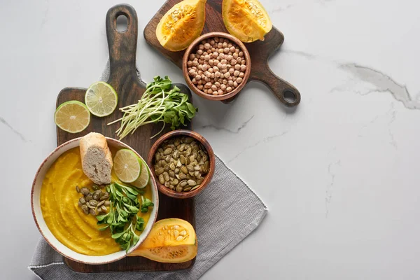 Blick von oben auf schmackhafte pürierte Kürbissuppe auf Holzschneidebrett mit Zutaten auf Marmoroberfläche — Stockfoto