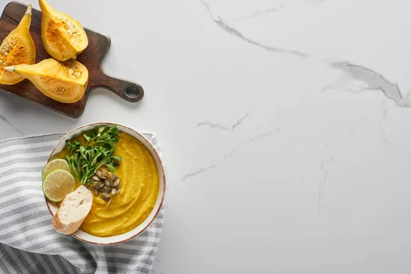 Vista dall'alto di gustosa zuppa di zucca schiacciata sul tagliere di legno con ingredienti sulla superficie di marmo — Foto stock