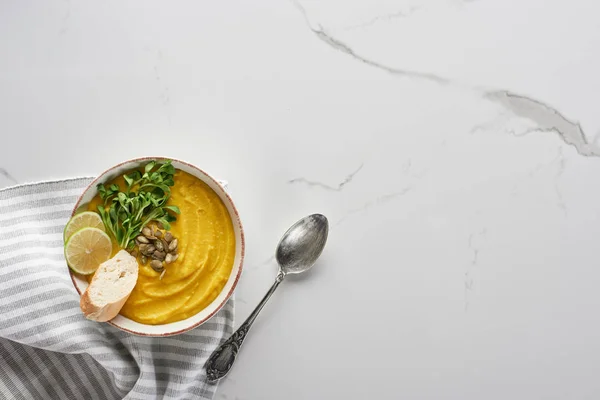 Vue de dessus de savoureuse purée de soupe de citrouille près de serviette rayée et cuillère en argent sur la surface du marbre — Photo de stock