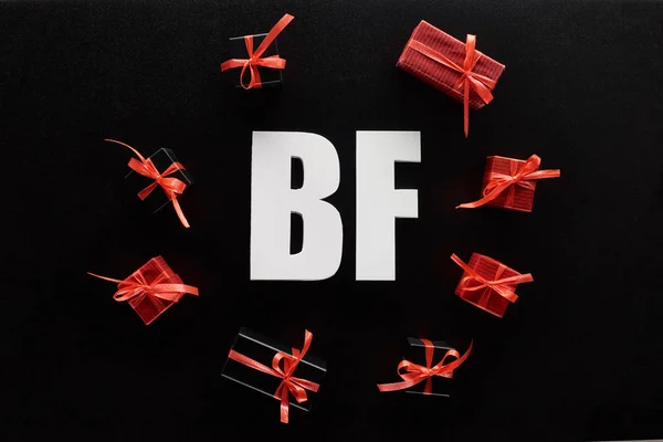 Vue de dessus du lettrage BF avec des cadeaux rouges isolés sur noir — Photo de stock