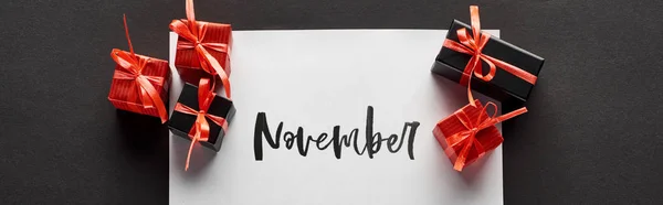 Top view of gift boxes and paper with November lettering on black background, panoramic shot — Stock Photo