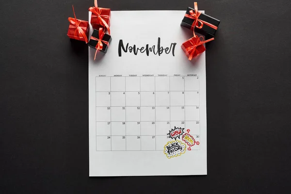 Top view of gift boxes and calendar with black Friday date on black background — Stock Photo