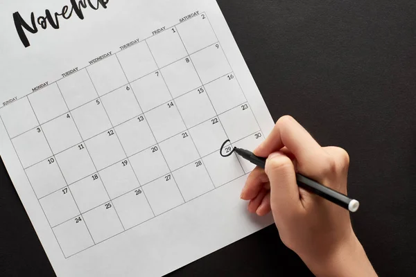 Vue recadrée de la femme marquant la date du vendredi noir dans le calendrier sur fond noir — Photo de stock