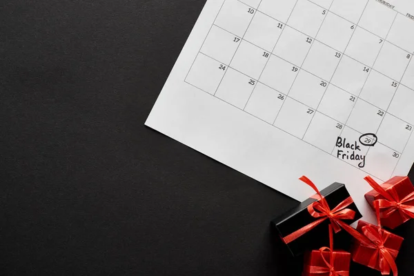 Top view of gift boxes and calendar with black Friday date on black background — Stock Photo