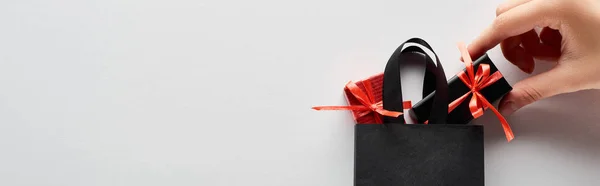 Vista cortada de mulher colocando pequenas caixas de presente em saco de compras preto no fundo branco, tiro panorâmico — Fotografia de Stock