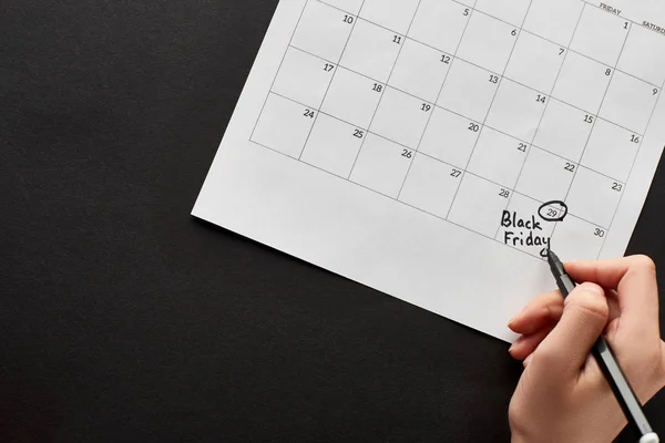 Teilansicht einer Frau, die das Datum des Black Friday im Kalender auf schwarzem Hintergrund markiert — Stockfoto