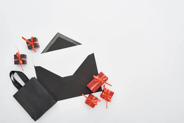 Vue du dessus de l'enveloppe noire avec carte blanche près des boîtes-cadeaux décoratives et du sac à provisions sur fond blanc — Photo de stock