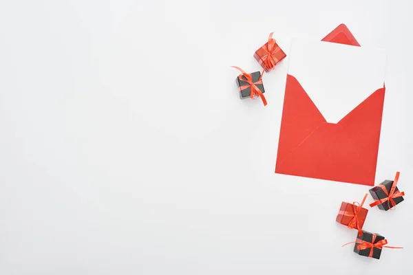 Top view of red envelope with blank card near decorative gift boxes on white background — Stock Photo