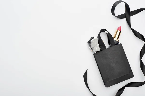 Top view of small shopping bag with male wristwatch and female lipstick near ribbon on white background — Stock Photo