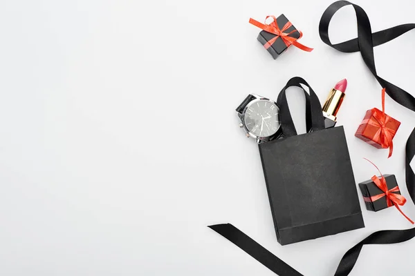 Top view of small shopping bag with male wristwatch and female lipstick near ribbon and presents on white background — Stock Photo