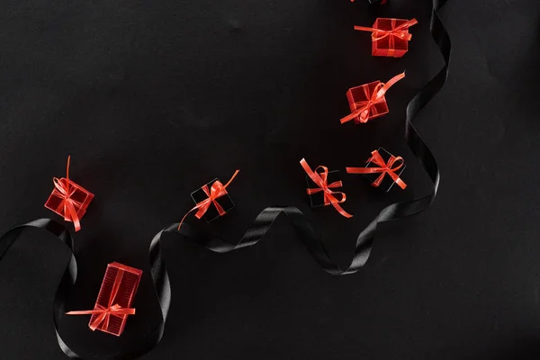 Vue de dessus des boîtes-cadeaux décoratives noires et rouges avec des arcs près du ruban sur fond noir — Photo de stock