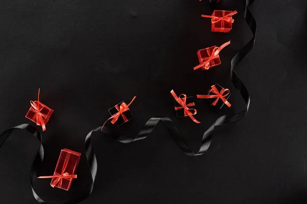 Top view of black and red decorative gift boxes with bows near ribbon on black background — Stock Photo