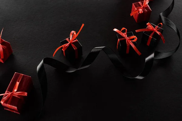 Vista superior de cajas de regalo decorativas negras y rojas con lazos cerca de la cinta sobre fondo negro - foto de stock
