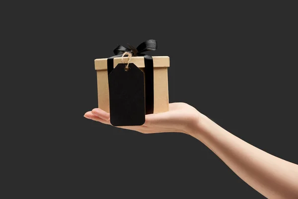 Cropped view of woman holding gift box with black blank label in hand isolated on black — Stock Photo