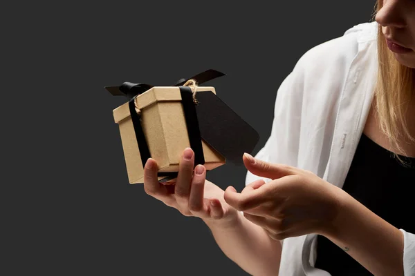 Cropped view of woman holding gift box with black blank label in hand isolated on black — Stock Photo