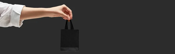 Recortado vista de la mujer sosteniendo pequeña bolsa de compras negro en mano aislado en negro, tiro panorámico - foto de stock