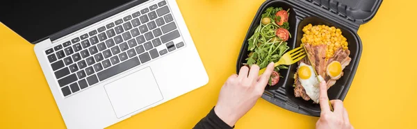 Tiro panorâmico de mulher comendo de pacote ecológico com carne, ovos fritos e salada isolada em amarelo — Fotografia de Stock