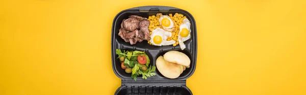 Панорамний знімок екологічного пакету з кукурудзою, м'ясом, смаженими яйцями, яблуками та салатом ізольовані на жовтому — стокове фото