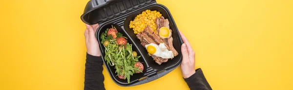 Tiro panorâmico de mulher segurando pacote ecológico com milho, carne, ovos fritos e salada isolada em amarelo — Fotografia de Stock