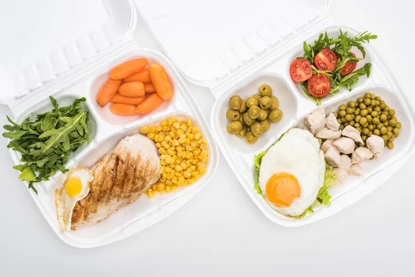 Vista superior de los paquetes ecológicos con rúcula, verduras, carne, huevos fritos y ensalada sobre fondo blanco - foto de stock