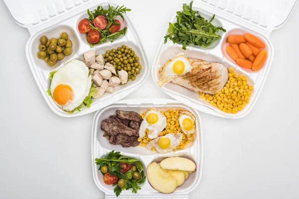 Vista dall'alto di confezioni ecologiche con mele, verdure, carne, uova fritte e insalate su sfondo bianco — Foto stock