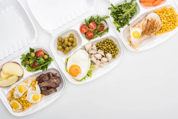 Вид сверху на экологические пакеты с яблоками, овощами, мясом, яичницей и салатами на белом фоне — стоковое фото