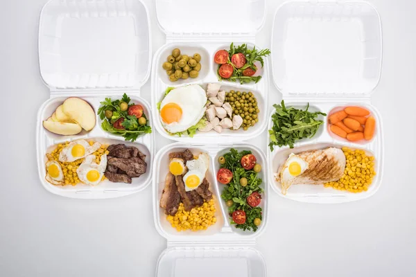 Vista superior de los paquetes ecológicos con manzanas, verduras, carne, huevos fritos y ensaladas sobre fondo blanco — Stock Photo