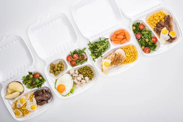 Vista superior de los paquetes ecológicos con manzanas, verduras, carne, huevos fritos y ensaladas sobre fondo blanco - foto de stock