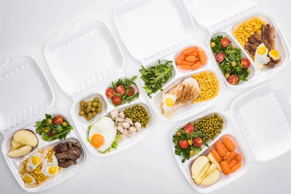 Vista superior de los paquetes ecológicos con manzanas, verduras, carne, huevos fritos y ensaladas sobre fondo blanco - foto de stock