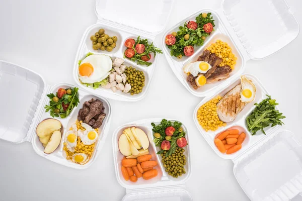 Vista superior de pacotes ecológicos com maçãs, legumes, carne, ovos fritos e saladas em fundo branco — Fotografia de Stock