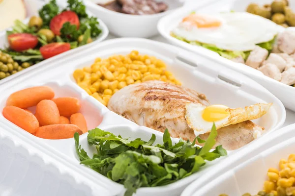 Вибірковий фокус екологічного пакету з овочами, м'ясом, смаженим яйцем і руколою на білому тлі — стокове фото