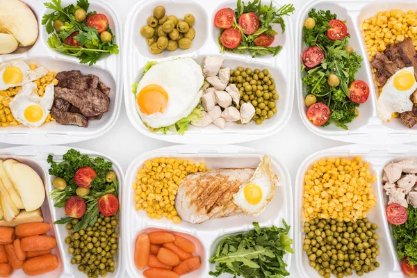 Vue du dessus des emballages écologiques avec pommes, légumes, viande, œufs frits et salades sur fond blanc — Photo de stock