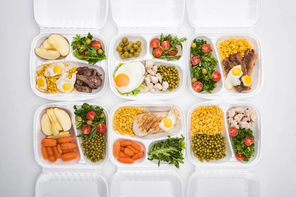 Вид сверху на экологические пакеты с яблоками, овощами, мясом, яичницей и салатами на белом фоне — стоковое фото