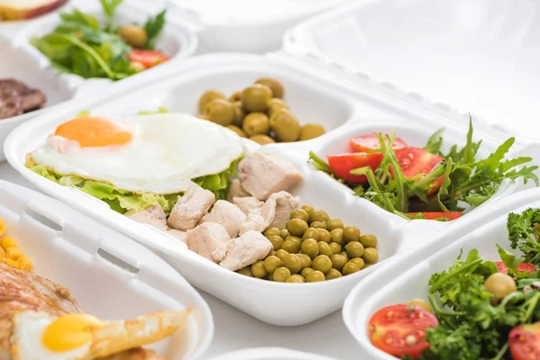 Foco seletivo do pacote ecológico com legumes, carne, ovo frito e salada no fundo branco — Fotografia de Stock