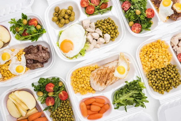 Vista superior de pacotes ecológicos com maçãs, legumes, carne, ovos fritos e saladas em fundo branco — Fotografia de Stock
