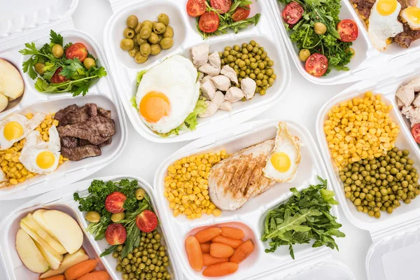 Vue du dessus des emballages écologiques avec pommes, légumes, viande, œufs frits et salades sur fond blanc — Photo de stock