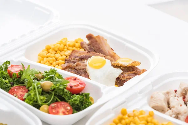 Enfoque selectivo del paquete ecológico con maíz, carne, huevo frito y ensalada sobre fondo blanco - foto de stock