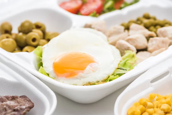 Вибірковий фокус екологічного пакету з овочами, м'ясом, смаженим яйцем та салатом на білому тлі — стокове фото