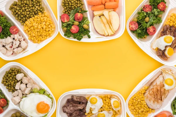 Vista dall'alto di confezioni ecologiche con mele, verdure, carne, uova fritte e insalate isolate su giallo — Foto stock